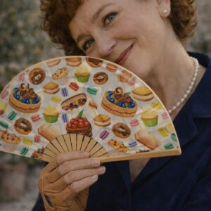 Femme élégante tenant un éventail Julia aux motifs pâtisserie colorés avec macarons et gâteaux dans une ambiance douce et lumineuse